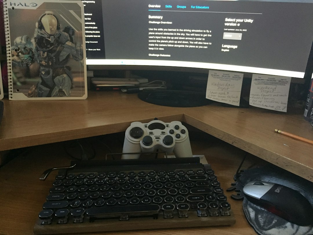 An office desk with a keyboard, monitor, mouse and a game controller on it