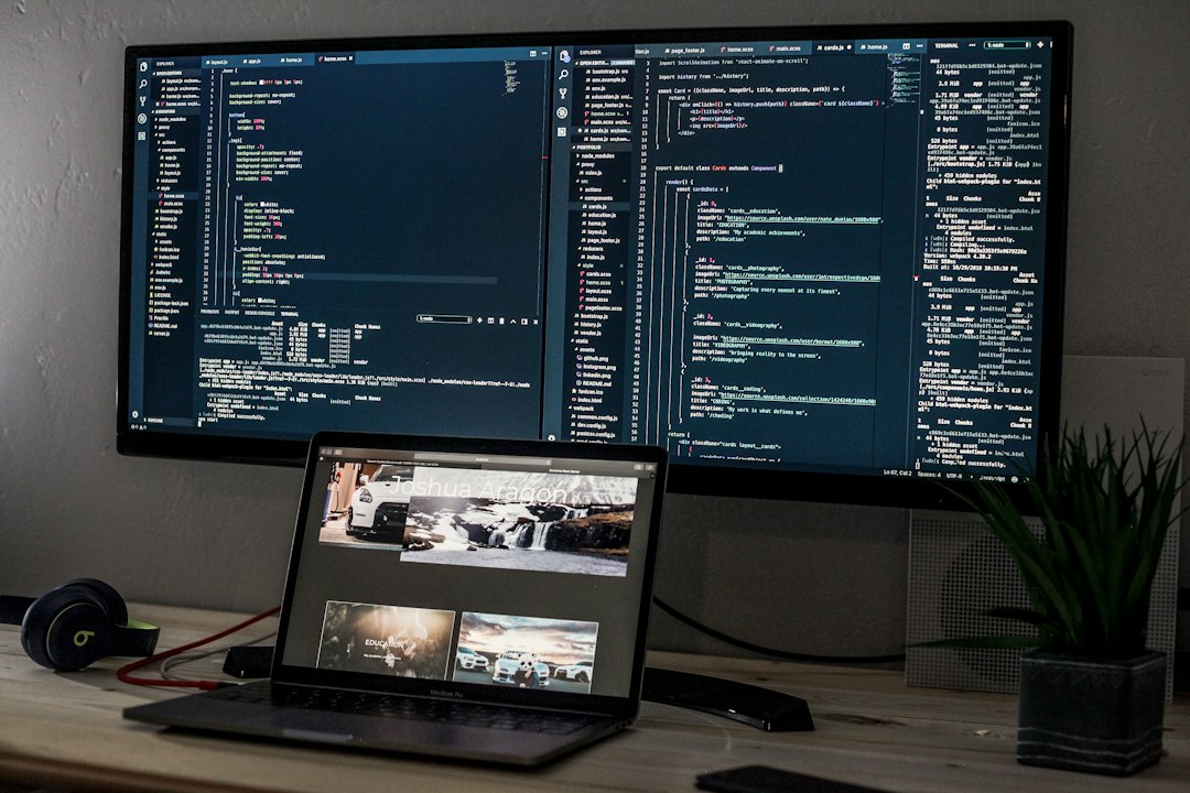 A laptop on a desk beside a wide monitor showing lines of code