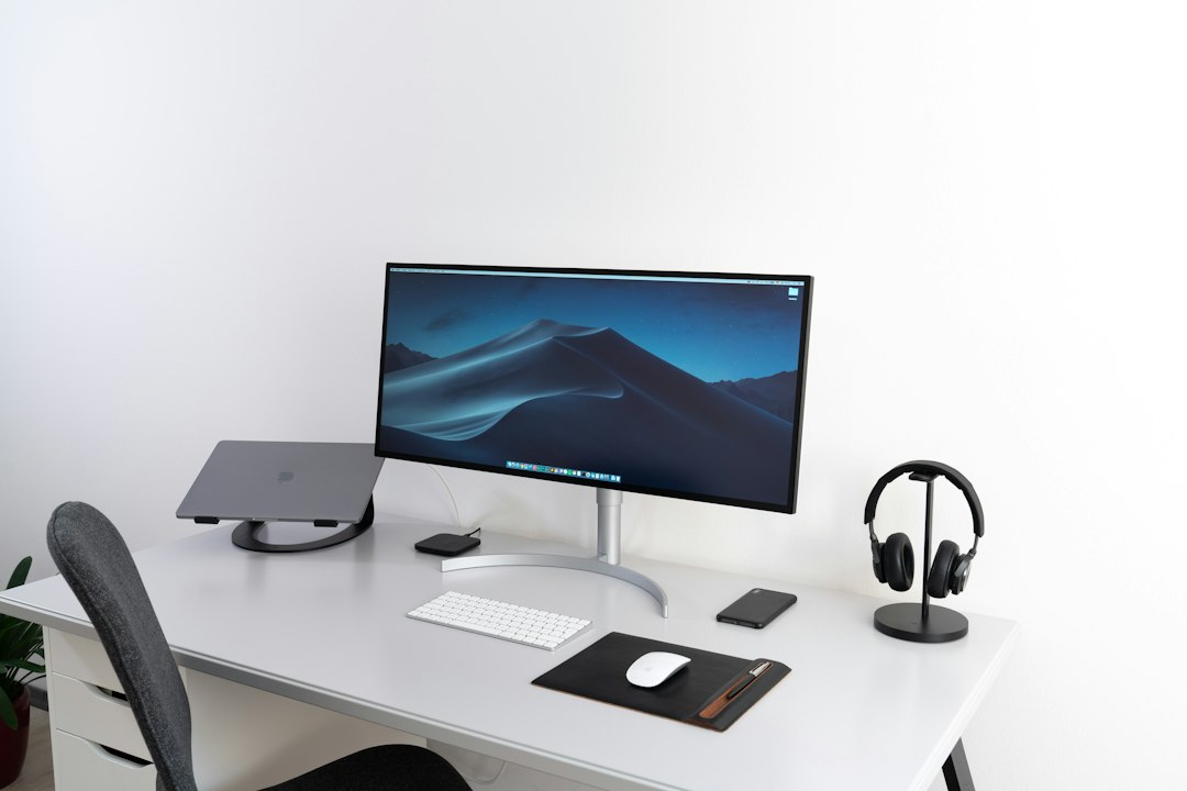 A black flat widescreen computer monitor on a wooden desk with a keyboard and mouse in front of it